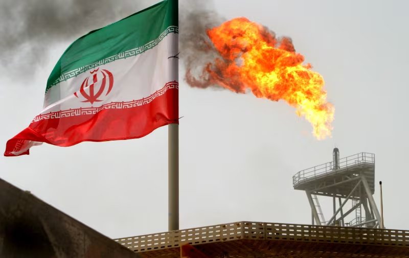 FOTO DE ARCHIVO: Una llamarada de gas en una plataforma de producción de petróleo se ve junto a una bandera iraní en el golfo. 25 de julio de 2005 
REUTERS/Raheb Homavandi