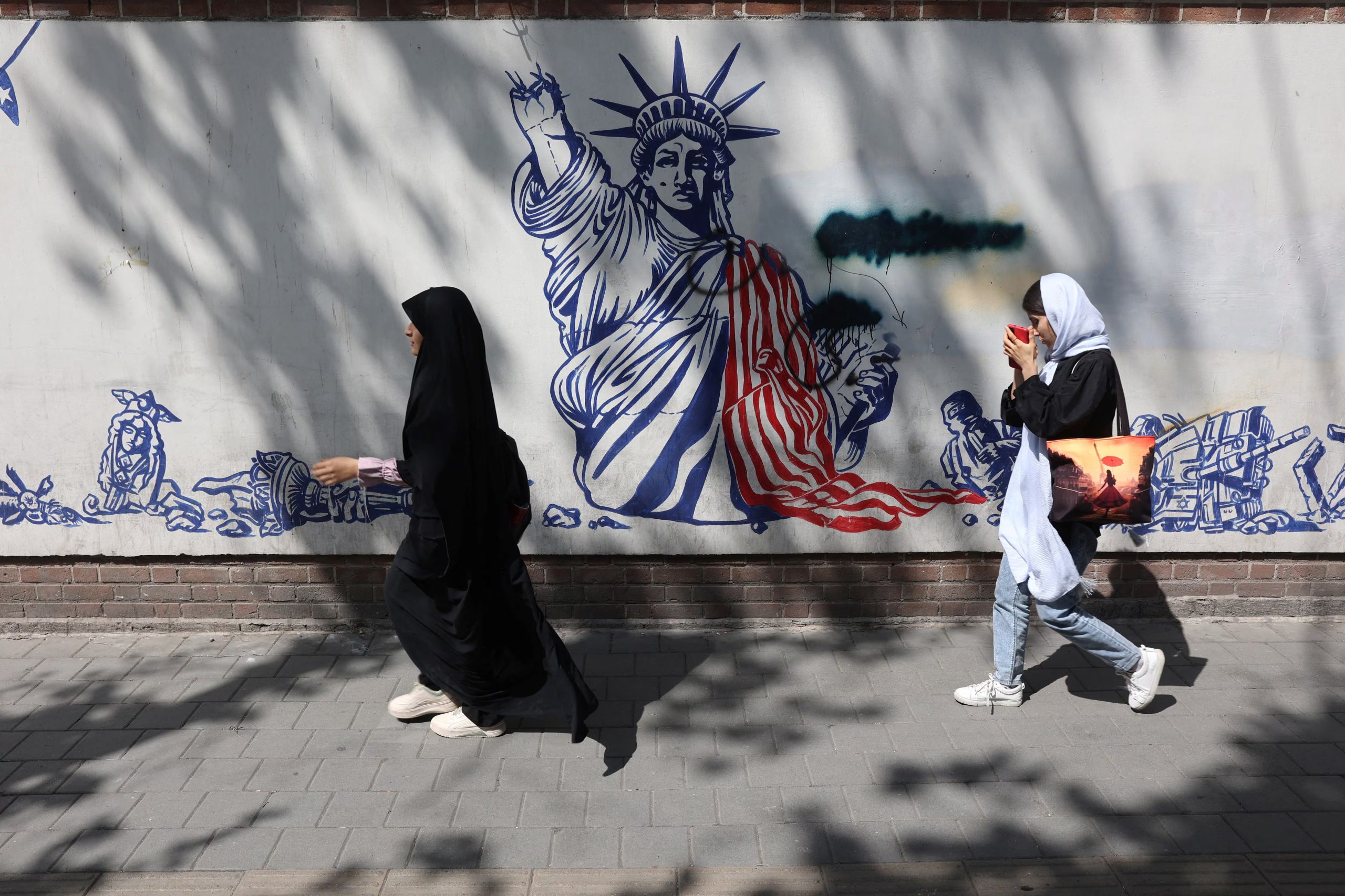 Personas caminan junto a un mural antiestadounidense en Teherán. La Guardia Revolucionaria lanzó una campaña de reclutamiento que incorpora a menores desde los 12 años para patrullar las calles de la capital durante la guerra. (Majid Asgaripour/WANA/REUTERS/archivo)