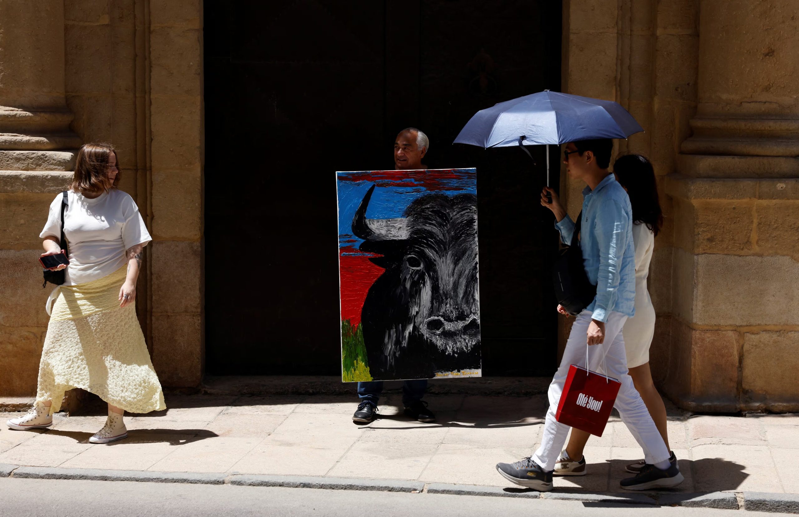El artista español Javier Toro Truncer posa con su obra recién pintada frente a la plaza de toros de Ronda mientras turistas se protegen del sol con paraguas, en una jornada en que varias regiones de España batieron récords de temperatura para el mes de mayo. (REUTERS/Jon Nazca) 
