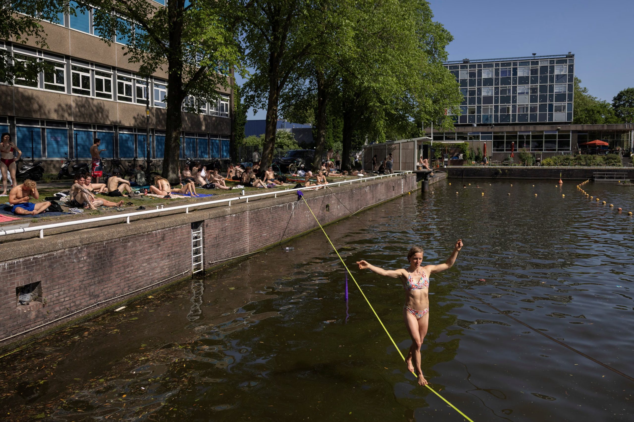 Bañistas disfrutan del sol en el Marineterrein de Ámsterdam mientras una mujer practica slackline sobre el agua, en una jornada de calor inusual para mayo en los Países Bajos, al norte del domo de calor que bate récords en Europa occidental. (REUTERS/Stelios Misinas) 