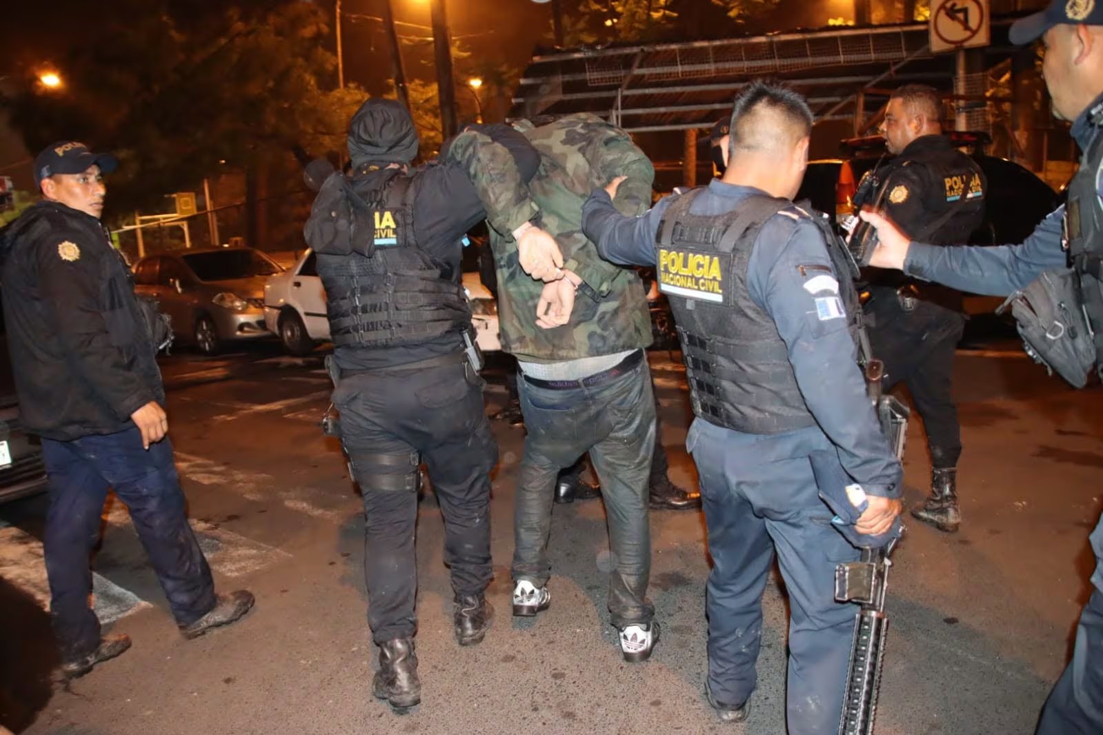 Agentes de la Policía Nacional Civil detienen a un hombre esposado durante un operativo nocturno en una calle poco iluminada. (PNCdeGuatemala)