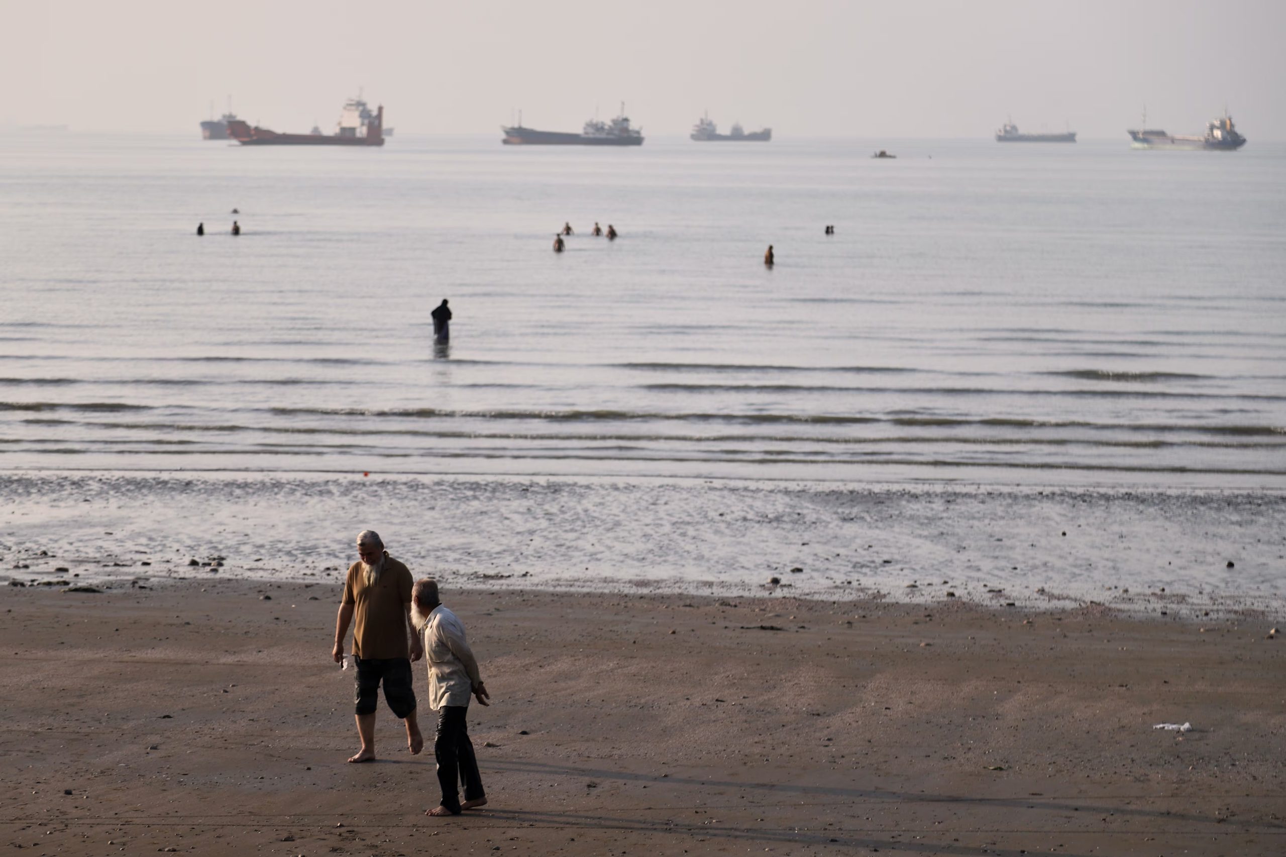 Bañistas en la costa de Bandar Abbas, Irán, con buques de carga anclados en el estrecho de Ormuz al fondo, el 1 de junio de 2026. El paso estratégico, por donde transita cerca del 20% del suministro mundial de petróleo, es uno de los principales puntos de tensión en la guerra entre EE.UU. e Irán. (Amirhosein Khorgooi/ISNA/AP)