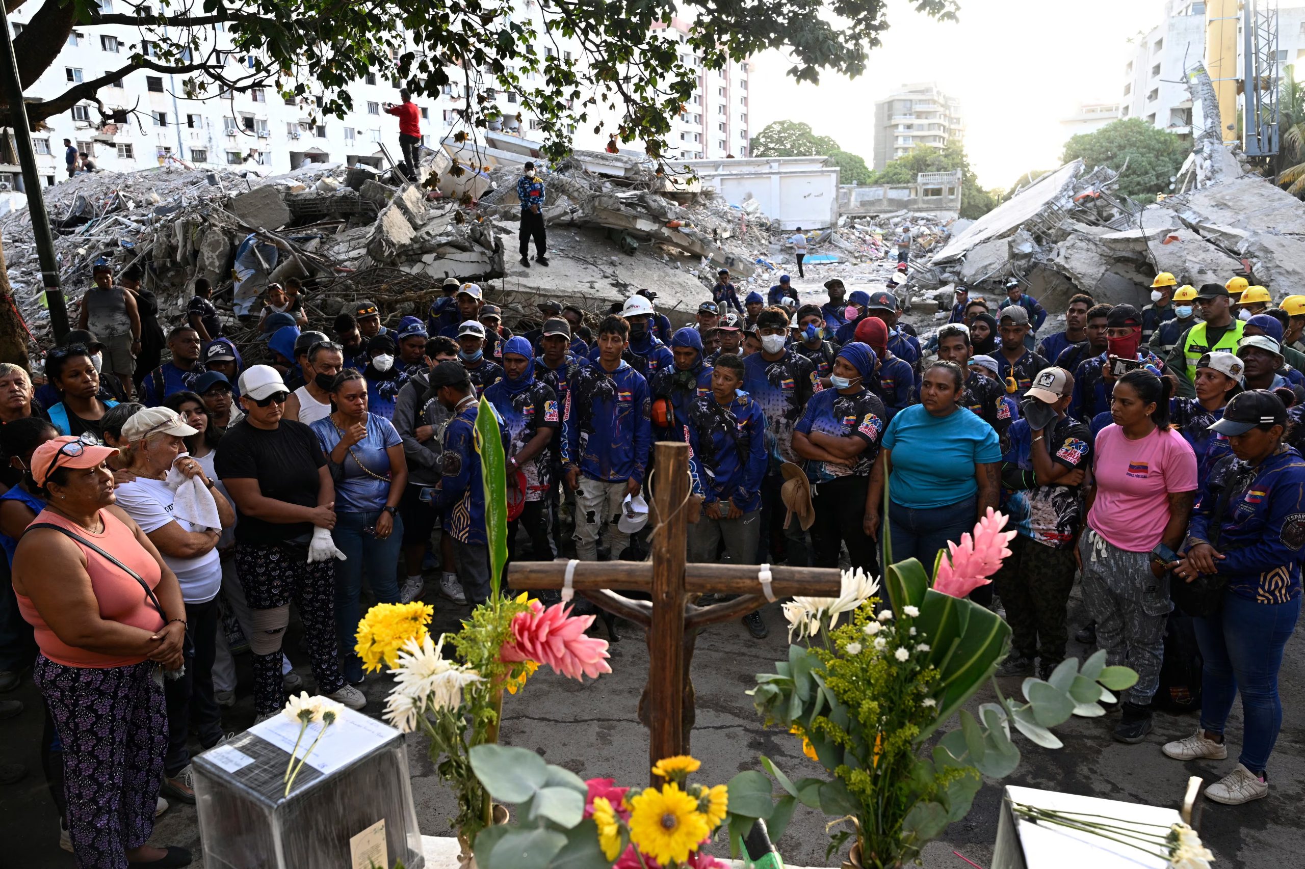 Familiares de víctimas, rescatistas y vecinos rinden homenaje a los fallecidos en Caraballeda, La Guaira, guardando un minuto de silencio frente a los restos de un complejo habitacional destruido (AFP)