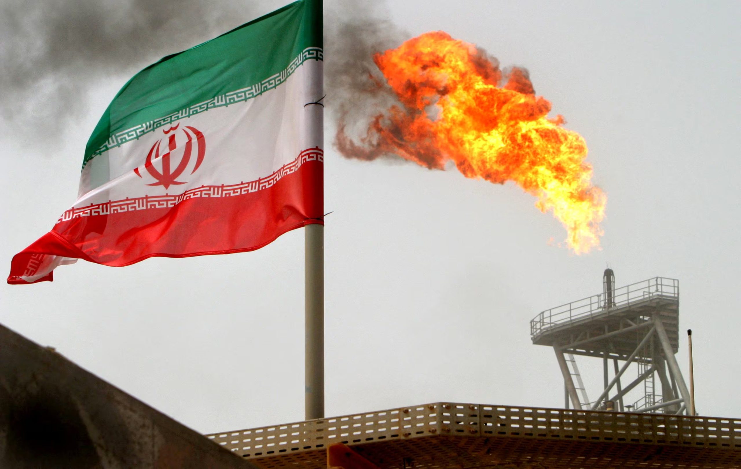 Una antorcha de gas arde en una plataforma de producción petrolera junto a una bandera de Irán en el golfo Pérsico (REUTERS/Archivo)