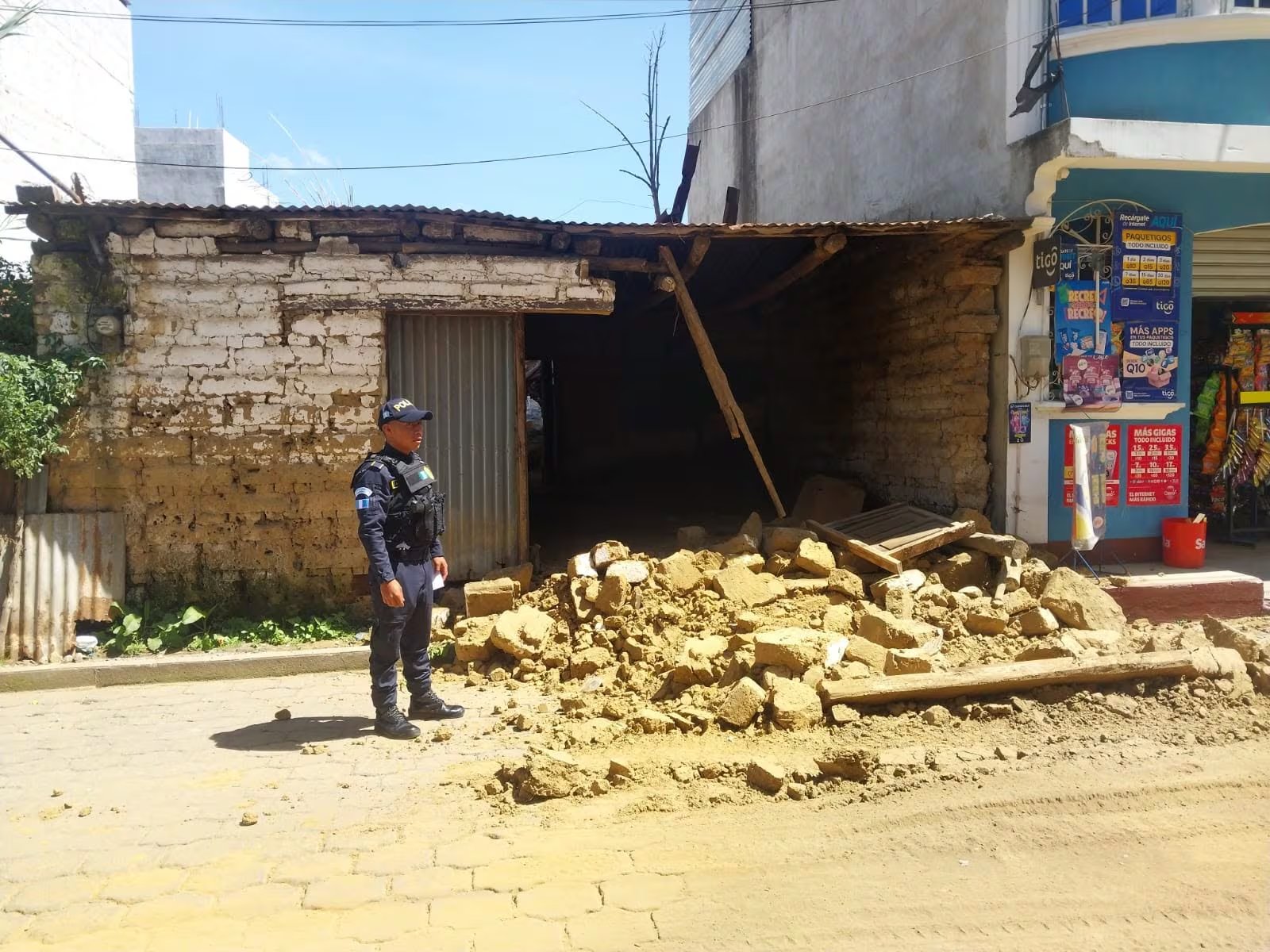 Un oficial de la Policía Nacional Civil se ubica frente a una vivienda parcialmente colapsada en Santa Clara La Laguna, con escombros de adobe y madera en el suelo. (PNCdeGuatemala)