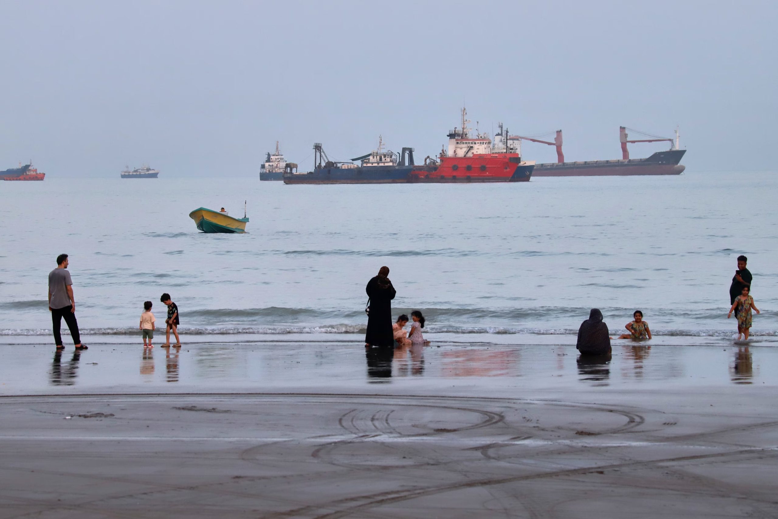 Personas disfrutan de la playa mientras al fondo se ven buques anclados en el estrecho de Ormuz, el miércoles 5 de agosto de 2026, frente a Bandar Abbas, Irán. (Amirhosein Khorgooi/ISNA via AP)