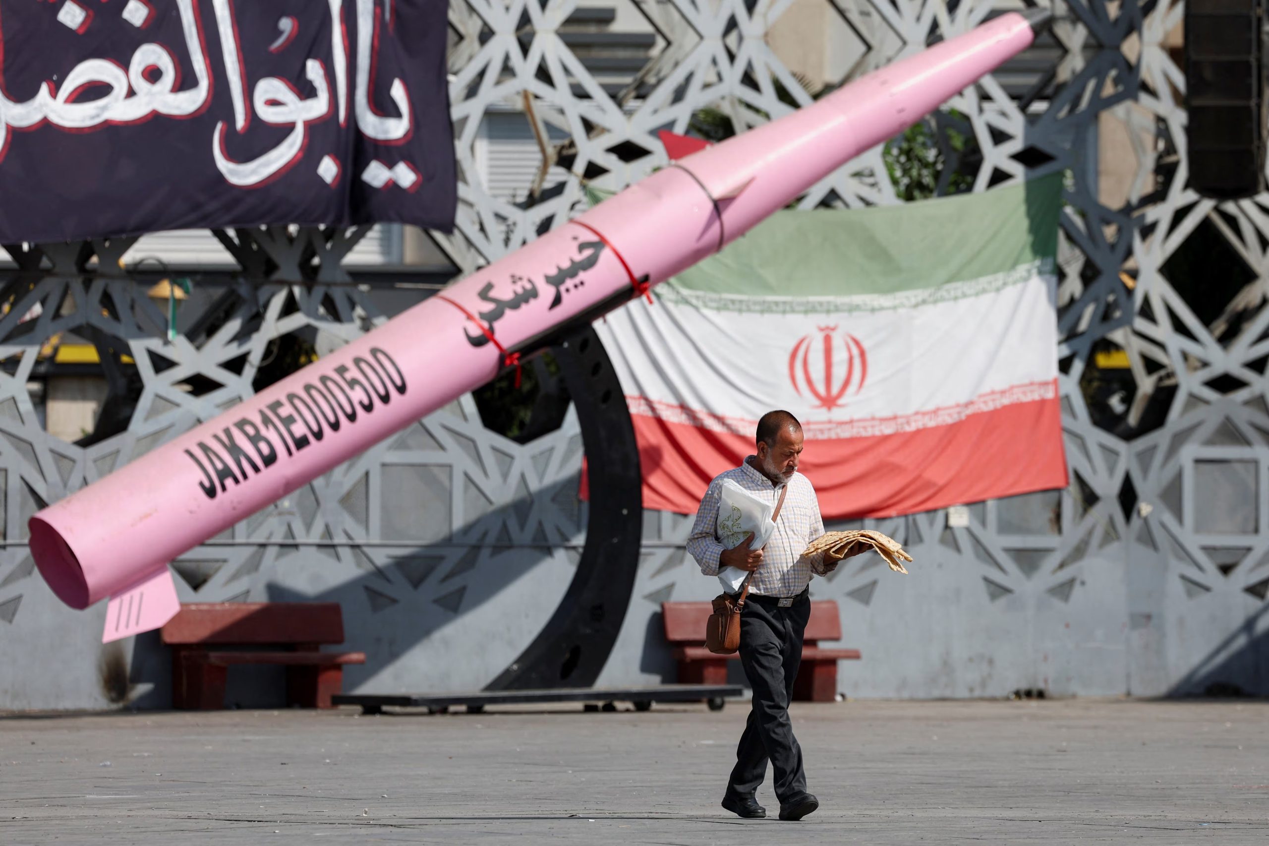Un hombre camina junto a una réplica simbólica de un misil iraní y una bandera iraní en la plaza del Imán Husein, en Teherán, Irán (Majid Asgaripour/WANA vía REUTERS)