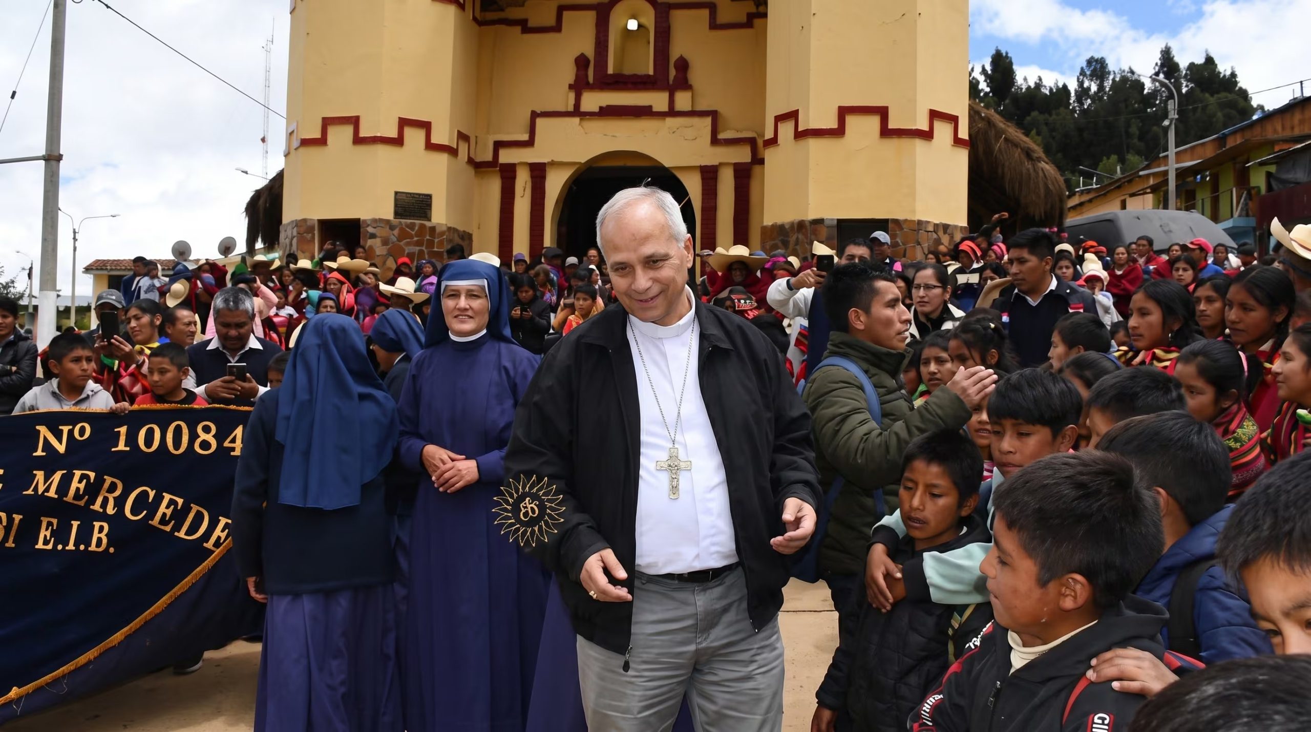 El papa León XIV, vestido de clergyman, saluda a la multitud de fieles que lo recibe junto a dos religiosas frente a una iglesia de color amarillo durante su visita pastoral en Chiclayo, Perú. (Andina Noticias)