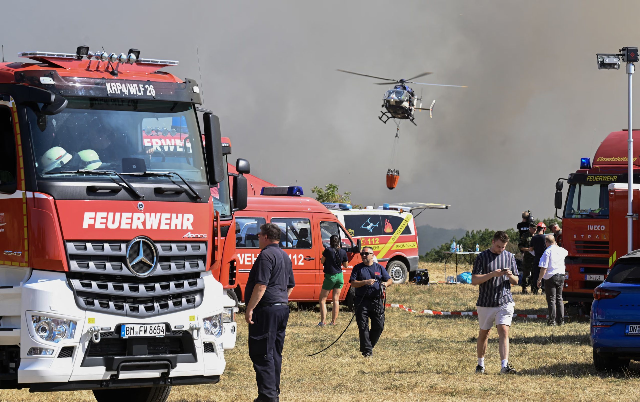 Un helicóptero de la policía carga agua para combatir un incendio forestal mientras los bomberos trabajan en Huertgenwald, en el oeste de Alemania. (Photo by Roberto Pfeil / AFP)