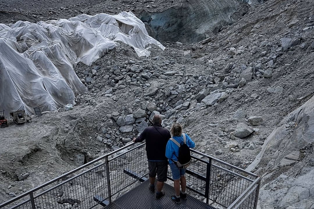 Dos personas miran desde un mirador metálico las lonas protectoras instaladas sobre el glaciar Mer de Glace. (AP Photo/Laurent Cipriani)