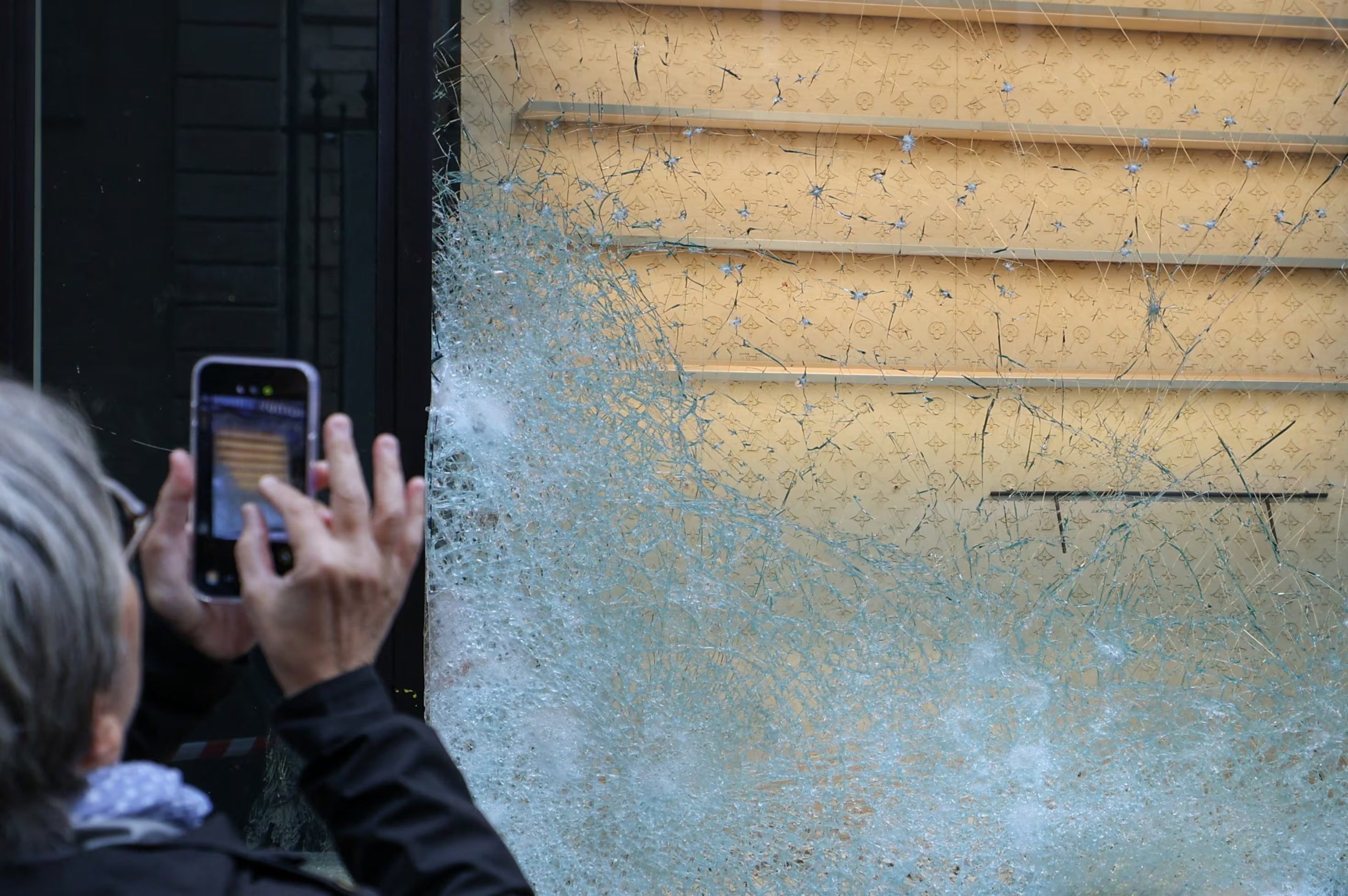 Una persona utiliza un teléfono móvil para fotografiar el escaparate roto de una tienda Louis Vuitton, al día siguiente de los enfrentamientos ocurridos durante una jornada nacional de manifestaciones contra el costo de la vida y el aumento de los precios del combustible en Francia, el 18 de octubre de 2026 (REUTERS/Manon Cruz)