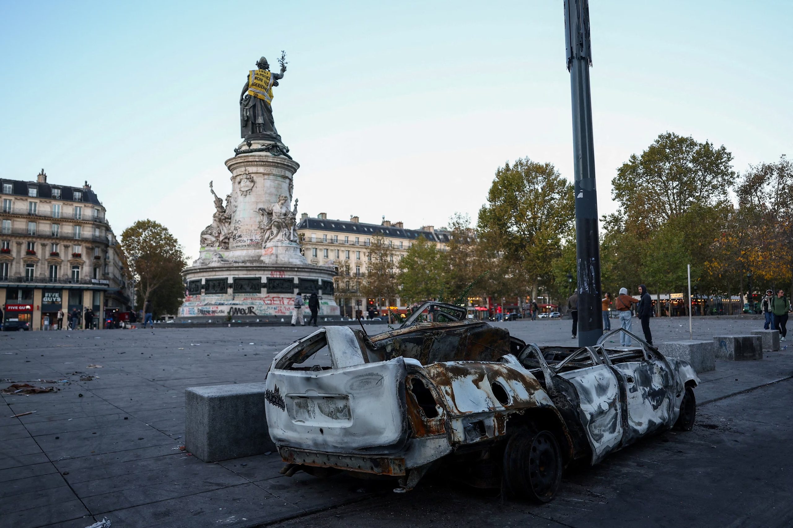 Un coche destrozado cerca de la estatua de Marianne en la Plaza de la República, con un chaleco amarillo encima, al día siguiente de los enfrentamientos ocurridos durante una jornada nacional de manifestaciones contra el coste de la vida y la subida de los precios del combustible, en París, Francia. 18 de octubre de 2026. En la parte trasera del chaleco se lee: 