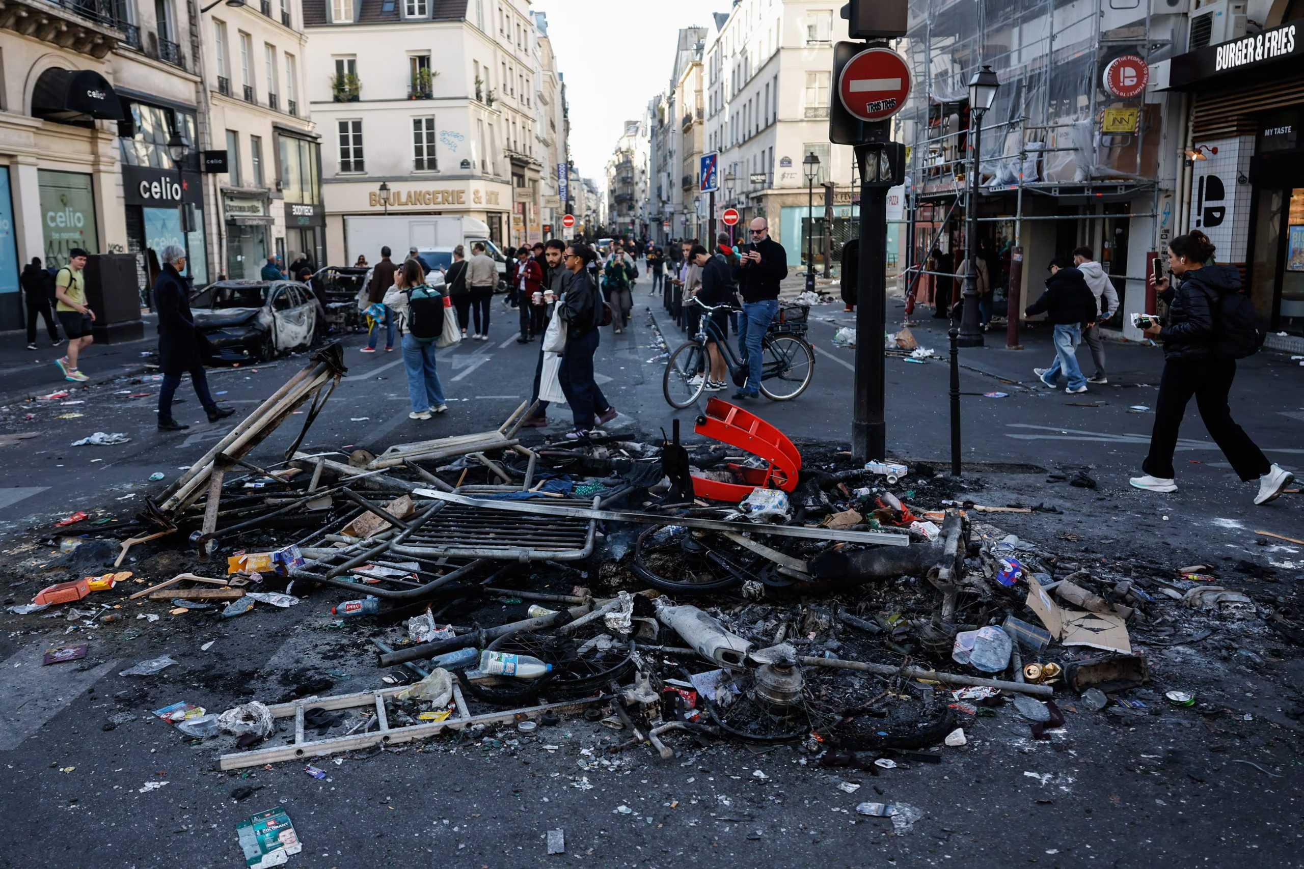 Unas personas pasan junto a los restos de una hoguera callejera tras los enfrentamientos entre la policía antidisturbios y los manifestantes en París, Francia, el 18 de octubre de 2026. EFE/EPA/MOHAMMED BADRA
