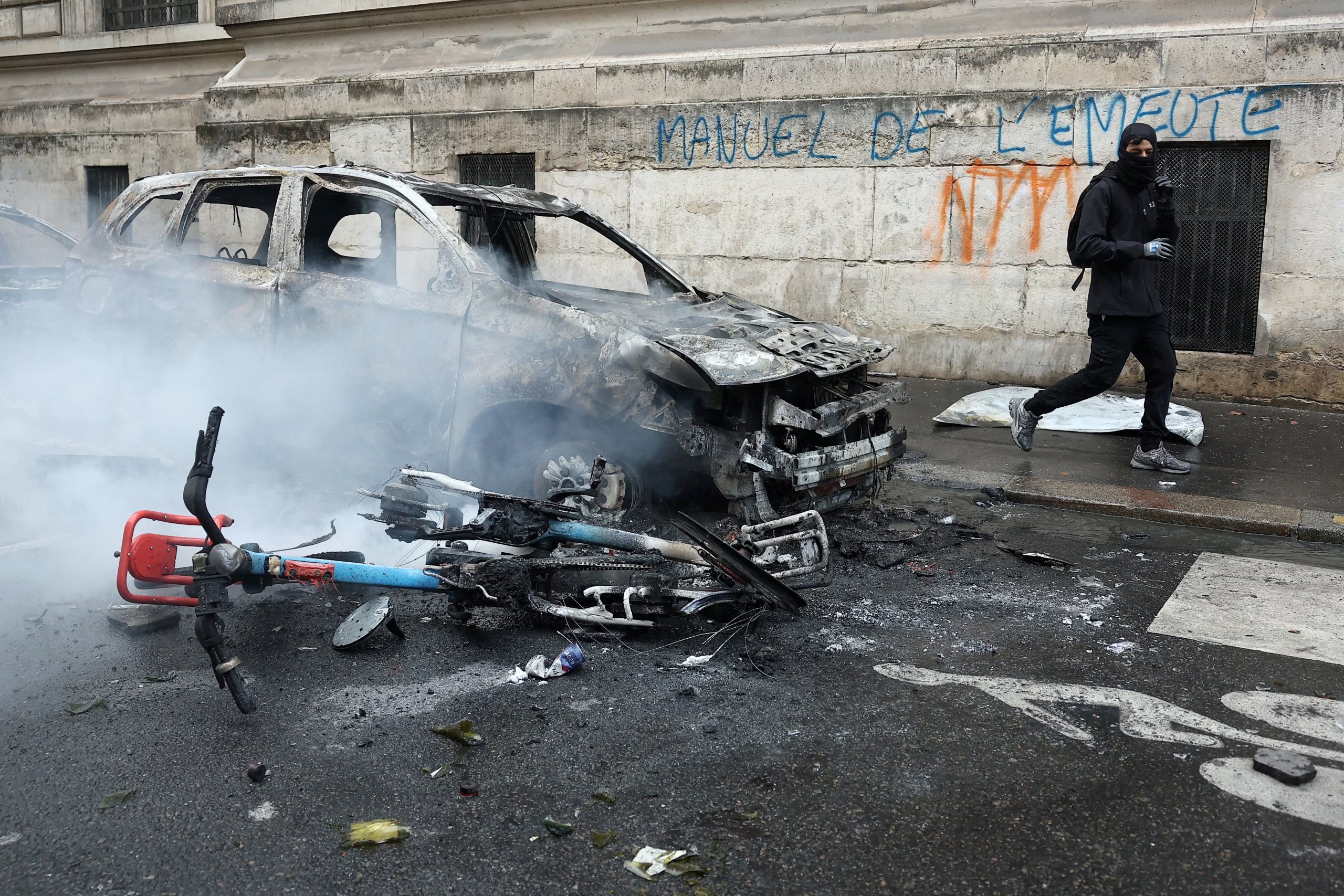 Un manifestante enmascarado pasa junto a un coche y una bicicleta calcinados durante una manifestación contra el coste de la vida y el aumento de los precios del combustible, cerca de la plaza de la República en París. La protesta forma parte de una movilización a escala nacional convocada por el movimiento de los «chalecos amarillos», a la que se sumaron estudiantes de secundaria y universitarios, profesores y padres —quienes exigen mejores condiciones escolares y medidas gubernamentales—, así como sindicatos, trabajadores, agricultores y jubilados. Francia, 17 de octubre de 2026. El lema que aparece en la pared dice: «Manual de disturbios». REUTERS/Abdul Saboor/Archivo