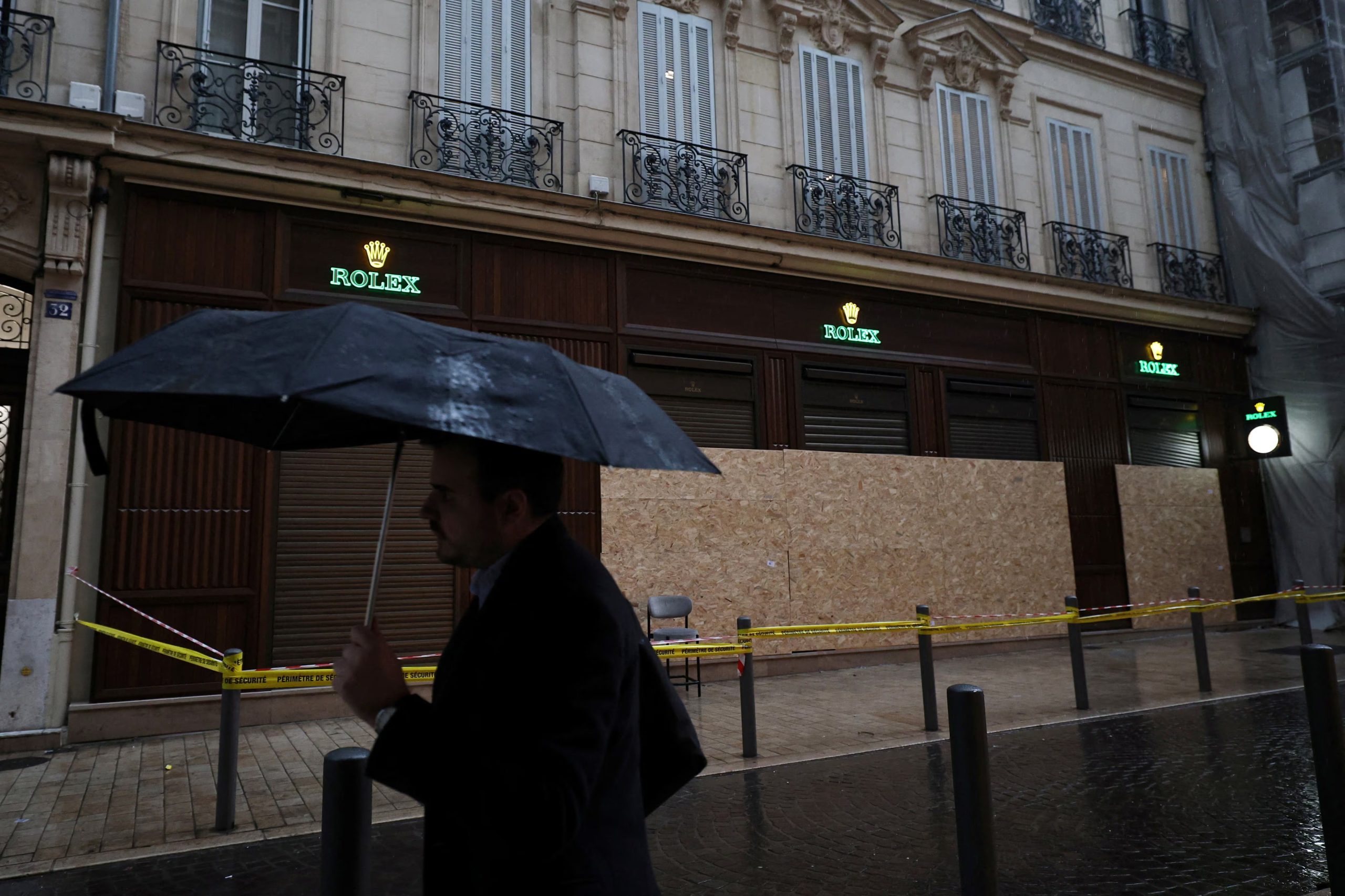 Un hombre se protege de la lluvia bajo un paraguas mientras pasa frente a una tienda Rolex vandalizada, con sus escaparates rotos tapiados tras los enfrentamientos que estallaron durante una jornada nacional de manifestaciones contra el costo de la vida y el aumento de los precios del combustible, en Marsella, Francia, el 19 de octubre de 2026. REUTERS/Manon Cruz