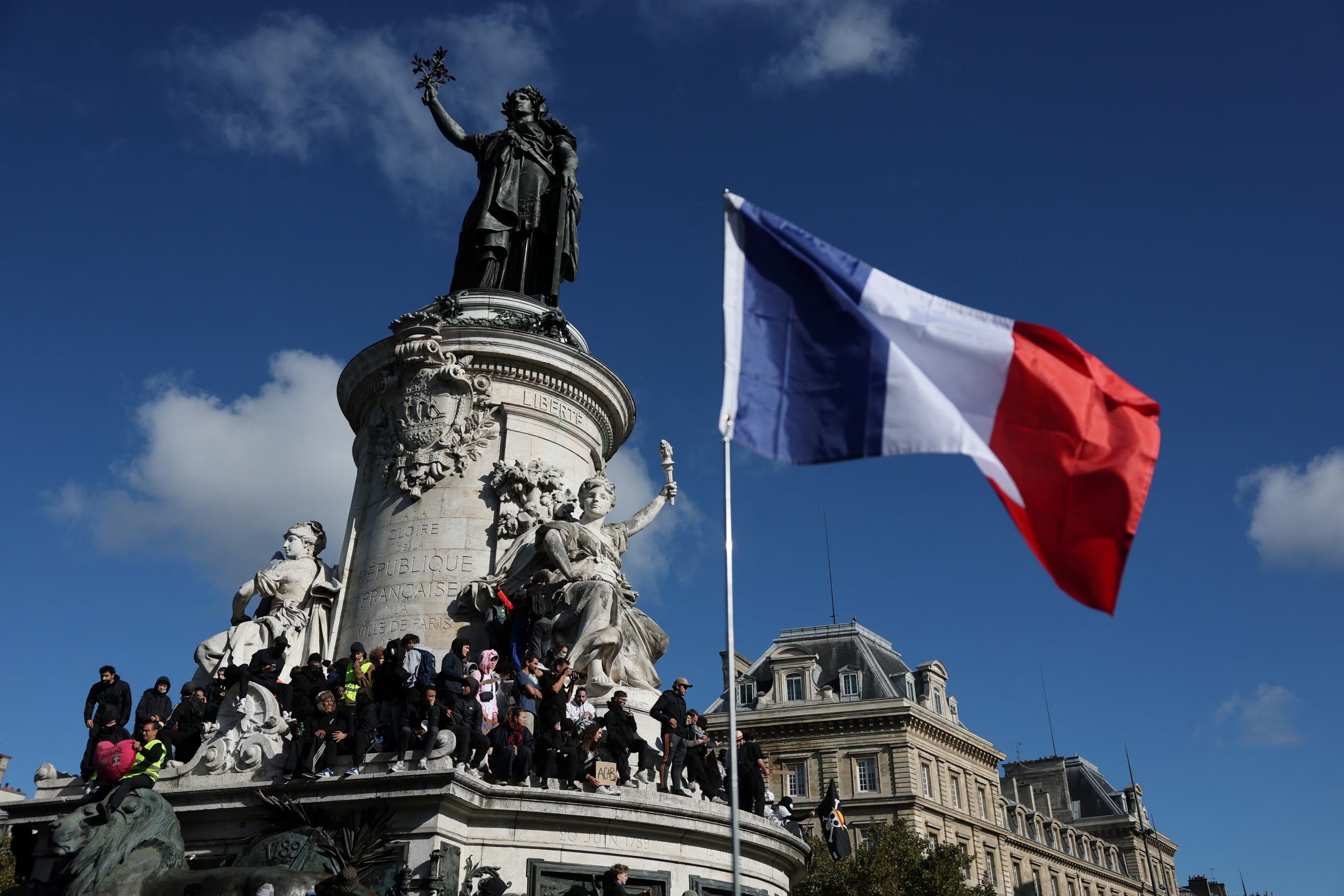 Una bandera francesa ondea mientras manifestantes se encuentran sobre la estatua de Marianne de la Plaza de la República durante una manifestación contra el costo de vida y el aumento de los precios de los combustibles en París, como parte de las protestas nacionales convocadas por el movimiento de los 