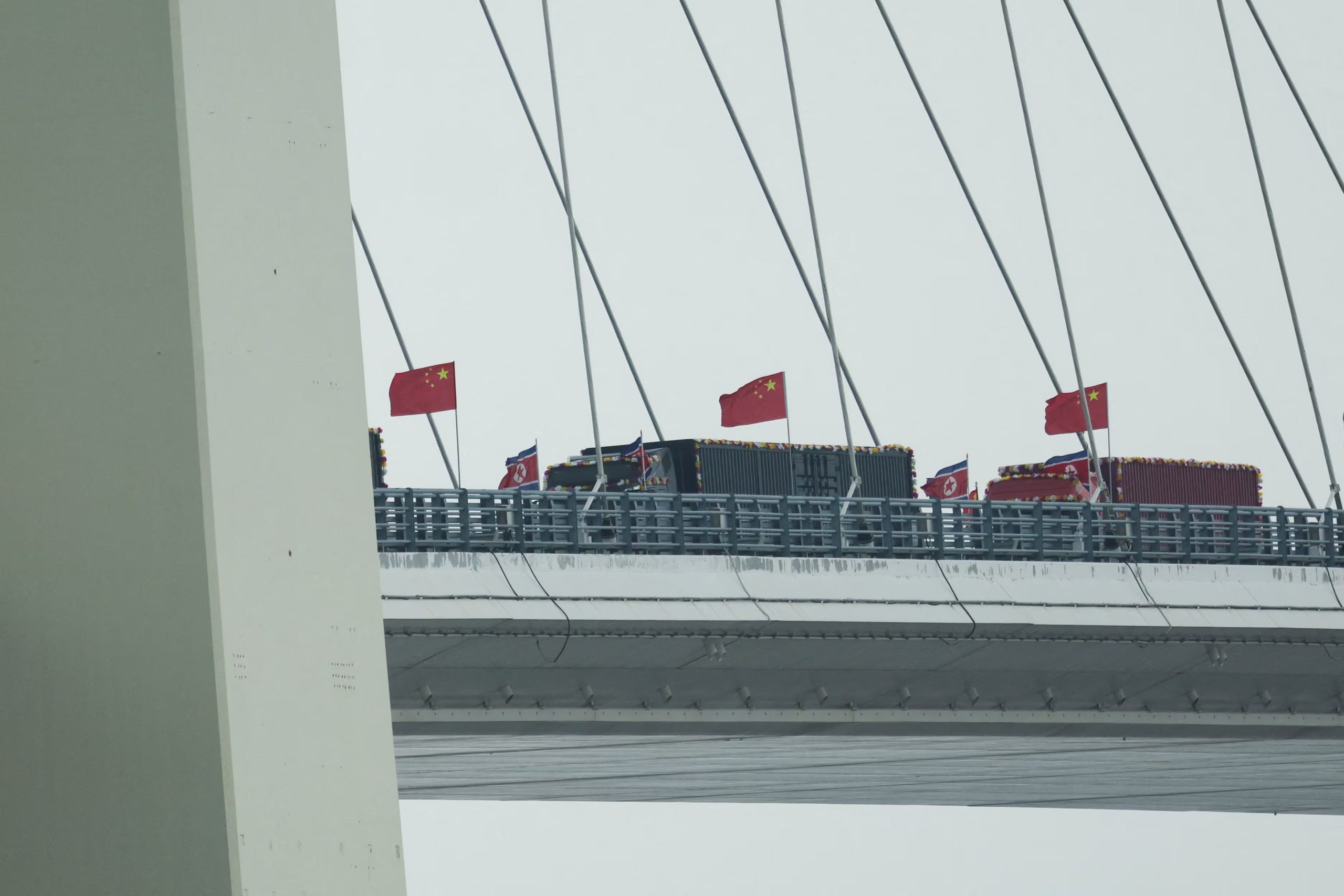 Camiones adornados con banderas norcoreanas entran al lado chino del recién inaugurado Puente del Nuevo Río Yalu, que conecta Sinuiju (Corea del Norte) con la Nueva Zona de Dandong (China) , el 15 de octubre de 2026 (REUTERS/Florence Lo)